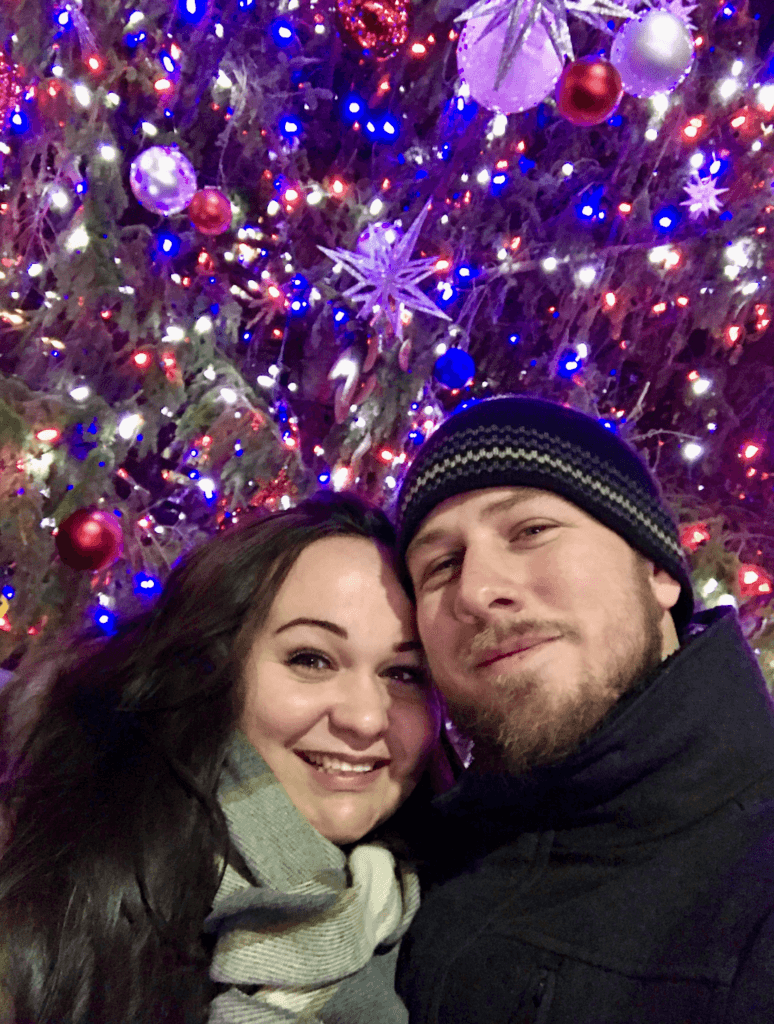 Ellie and her husband in front of the Bryant Park Christmas tree