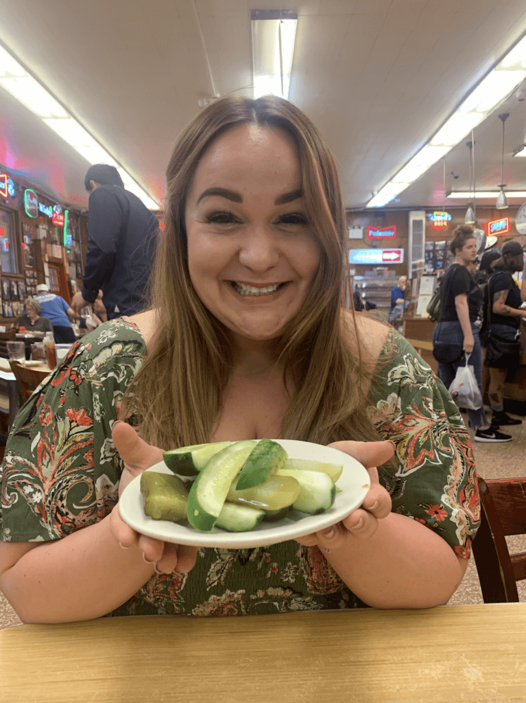 Ellie holding a plate of pickles in Katz's Deli