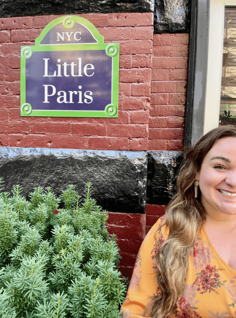 Ellie stood by the Little Paris sign in NYC