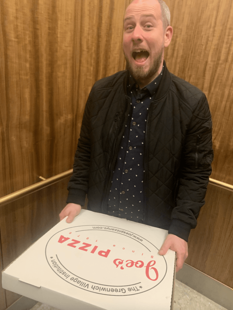 Ellie's husband holding a pizza box from Joe's pizza 